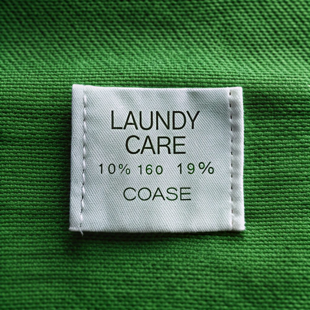 Étiquette d’entretien textile affichant le pictogramme de lavage en machine à 30 °C, posée près d’un lave-linge.